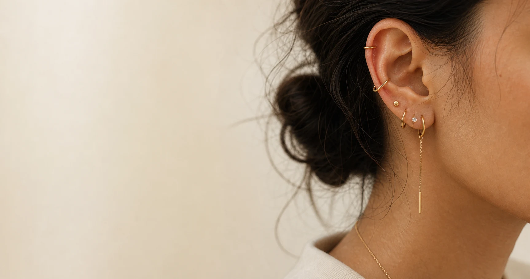 An editorial close-up of an ear styled with delicate gold hoops, cuffs, and studs